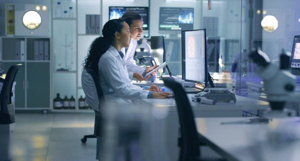 Medical researchers looking at and examining a brain scan on a computer while working late in an office together. Lab workers analyzing and talking about results from a checkup while working overtime